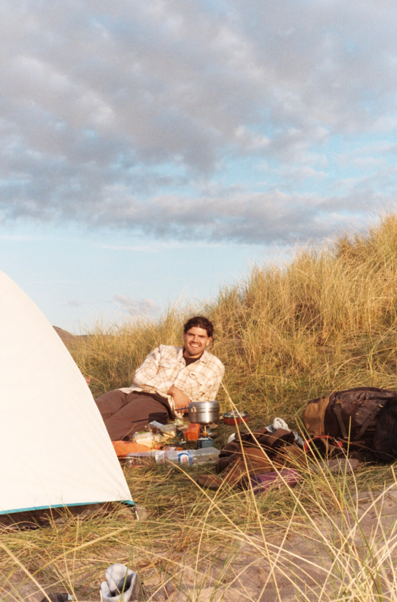 Joe relaxing beside a tent among coastal dunes